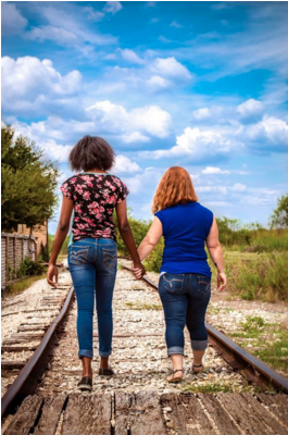 Image of two women walking hand in hand along a railway track during the day vibrant colours