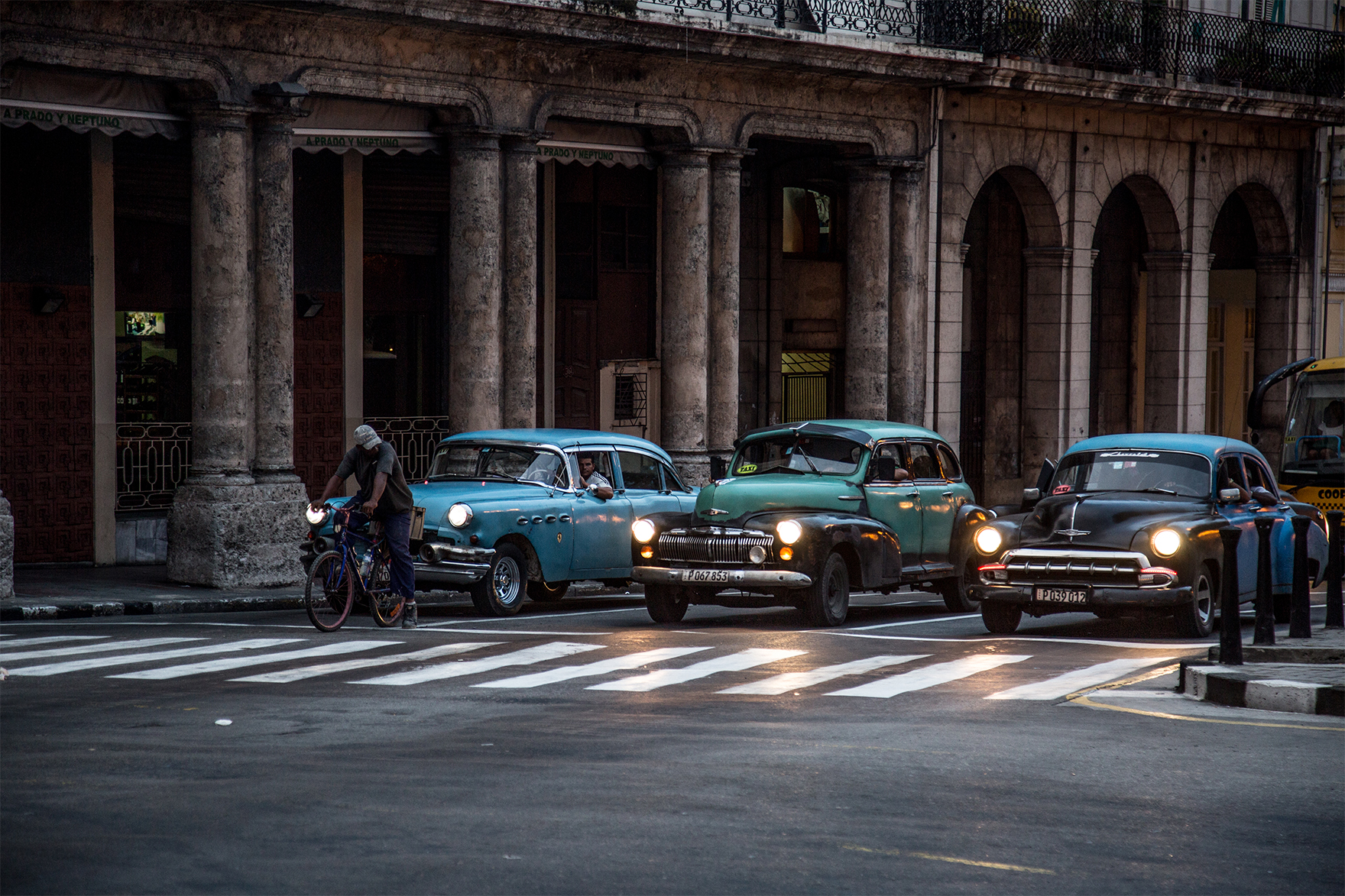 cuba vintage cars lined up at a zebra crossing in front of a portico