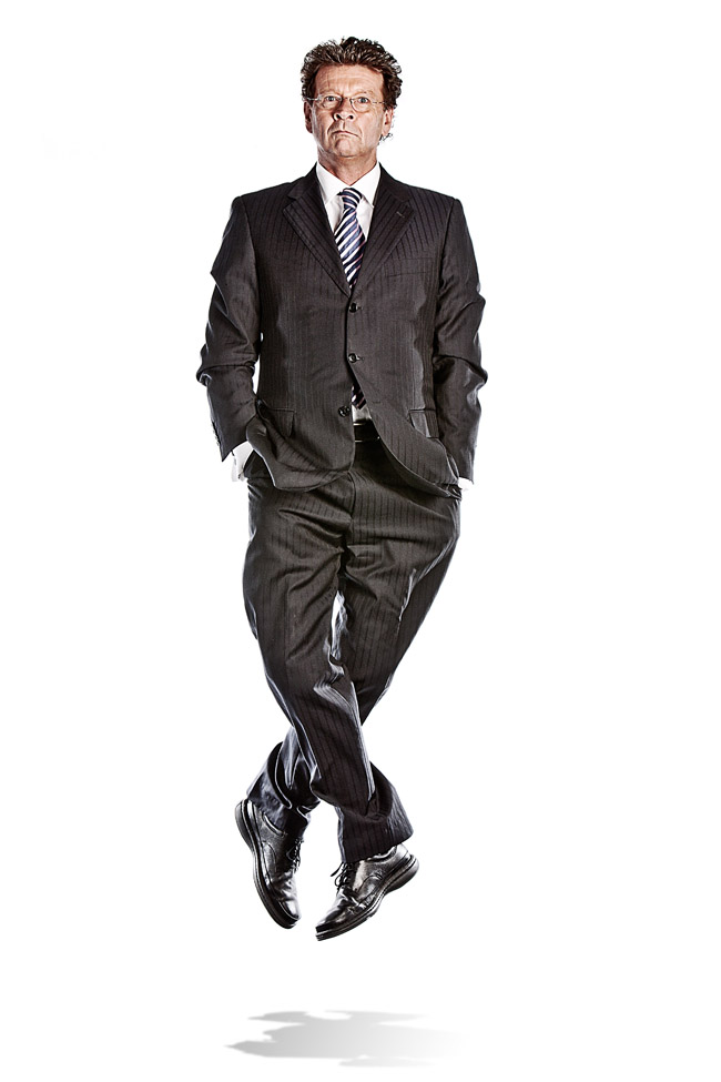 Comedian Red Symons jumping off the ground, legs crossed with a neutral expression