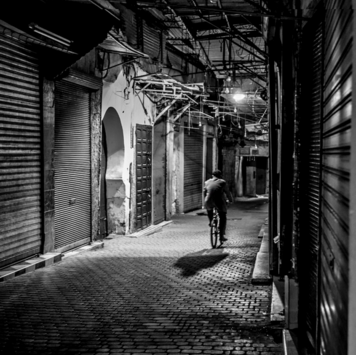 Street photo black and white person riding a bike down a narrow alley in Marrakesh