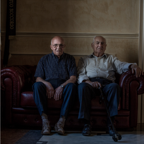 two men sitting on a couch by Gina Milicia
