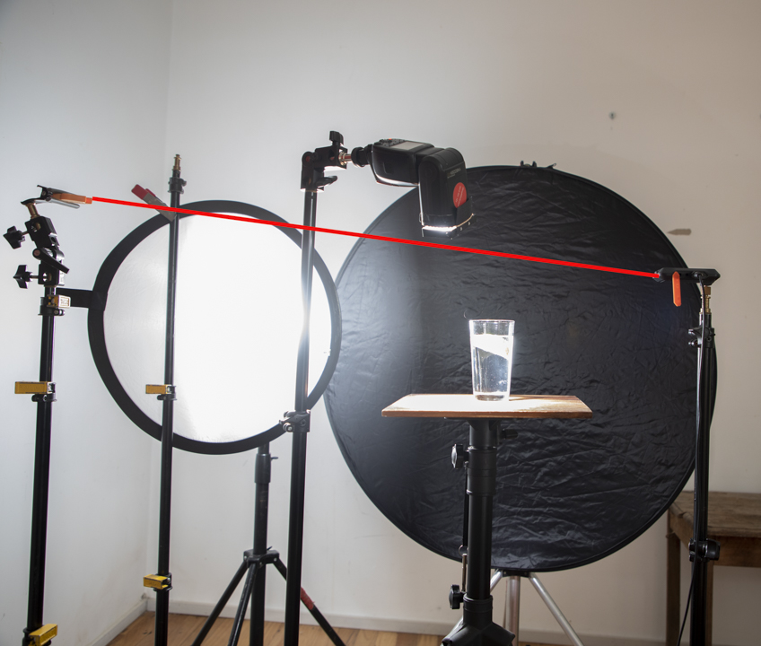 An image showing how this shot is taken using a laser trigger, black round background, glass on the table and a diffused light source. 