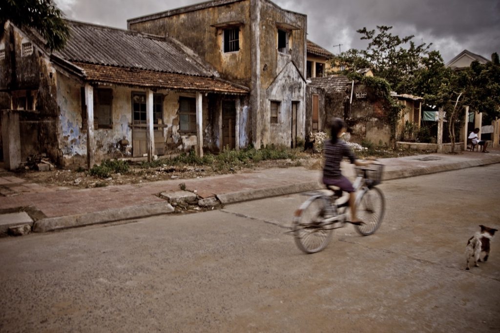 blurry woman on bike in front of dilapidated house
