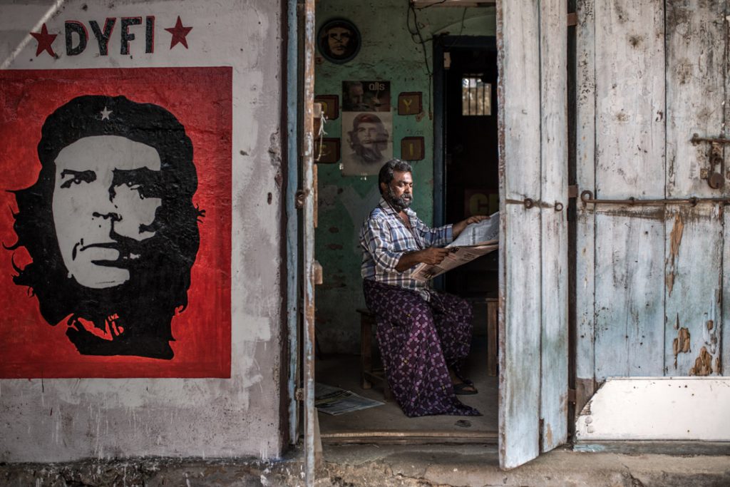 man reading newspaper with che guevera poster outside